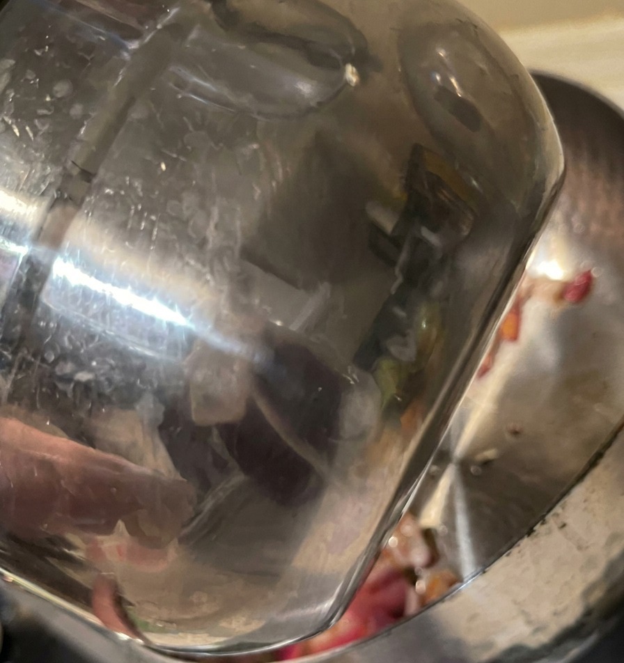 Acqua fresca versata da una tazza di acciaio in una pentola con cipolle rosse già soffritte.