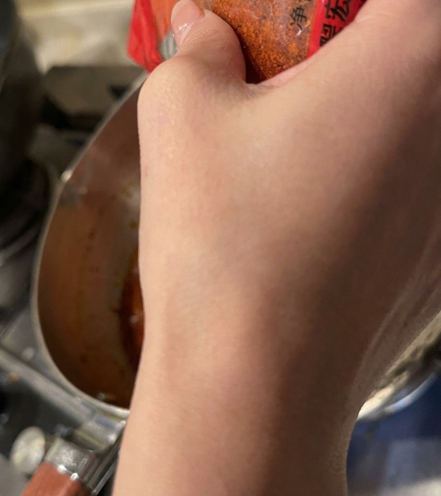 Peperoncino rosso in polvere versato nella zuppa arancione che inizia a sobbollire.