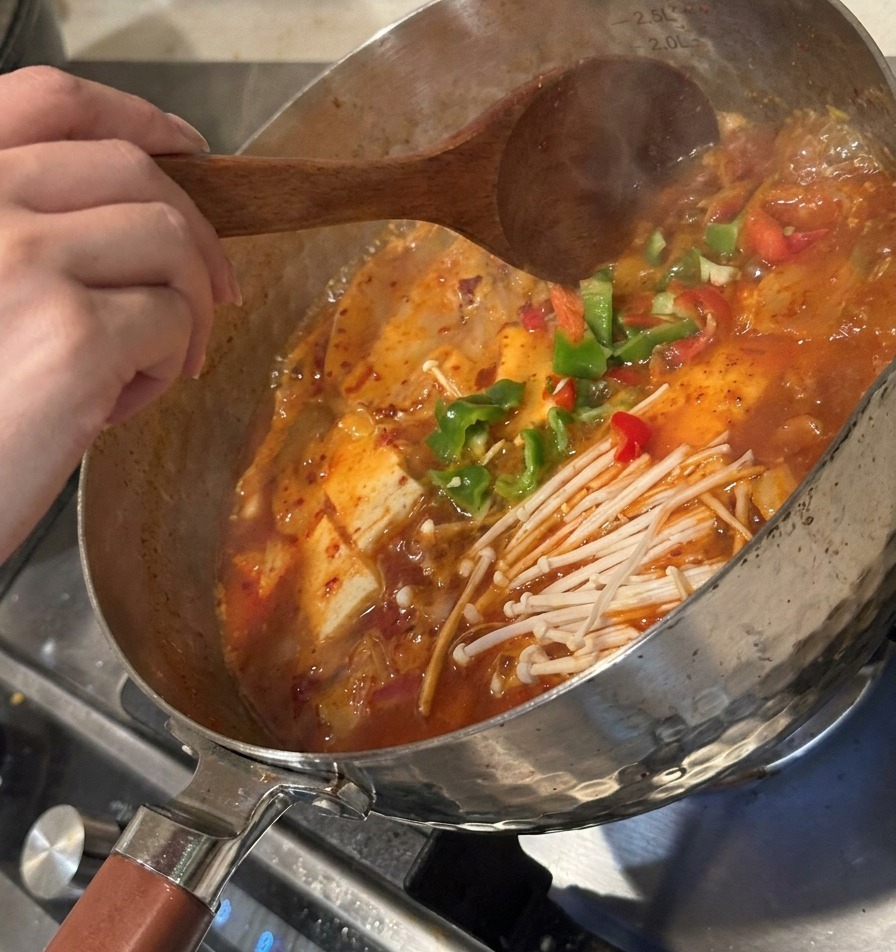 Peperoni verdi a fette e kimchi fermentato aggiunti alla zuppa che bolle, mescolando delicatamente.