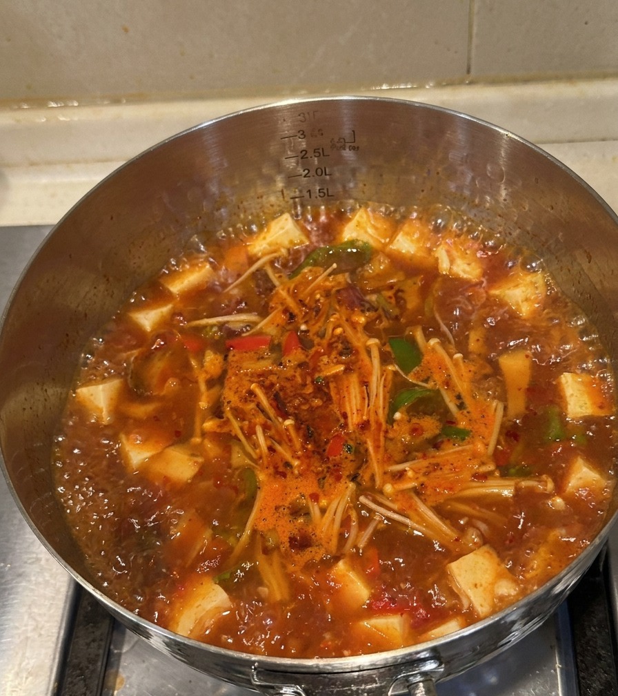 Pentola in acciaio con zuppa di kimchi e manzo pronta, con carne cotta, funghi e peperoni in evidenza.