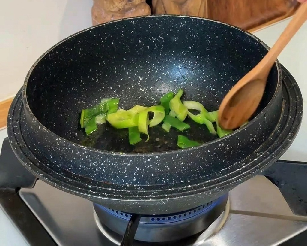 Cipollotti verdi tritati mescolati con un cucchiaio di legno in una pentola scura su un fornello a gas.
