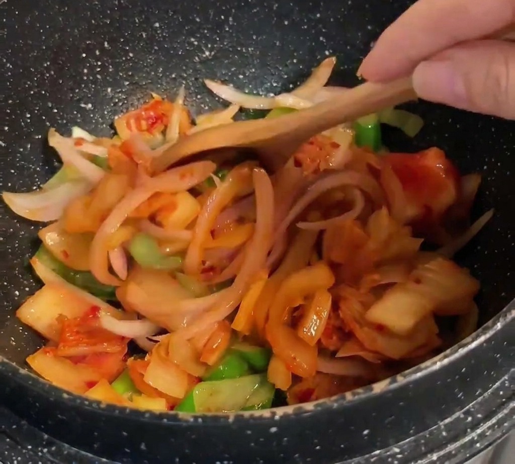 Un cucchiaio di legno che mescola kimchi arancione brillante a un mix di cipolle e cipollotti.