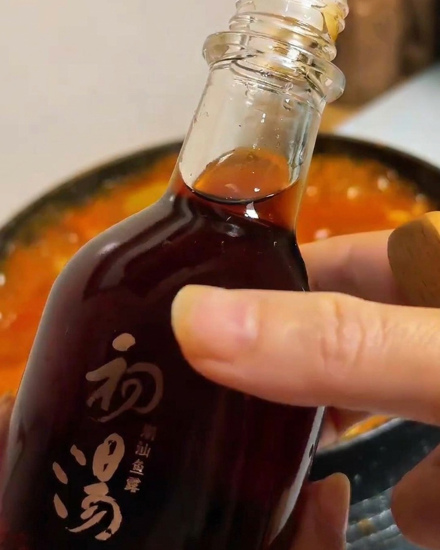 Una bottiglia di vetro scuro che versa salsa di pesce sapida in una pentola di stufato di tofu e verdure.