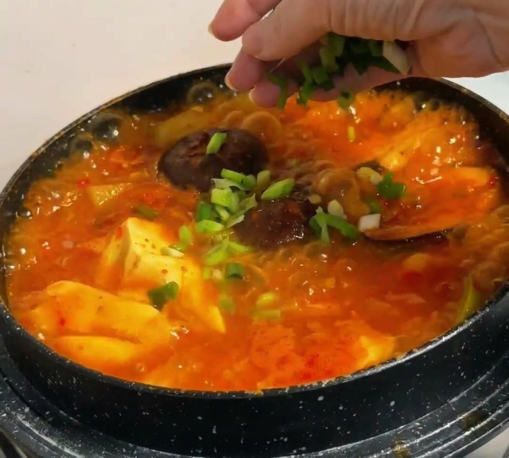 Cipollotti tritati spolverati a mano sopra uno stufato coreano rosso con tofu e funghi.