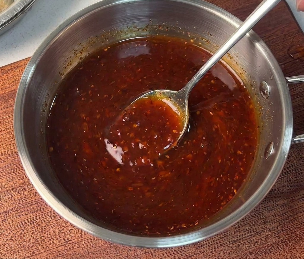 Una persona mescola una densa salsa rossa in una piccola ciotola dacciaio con un cucchiaio di metallo.
