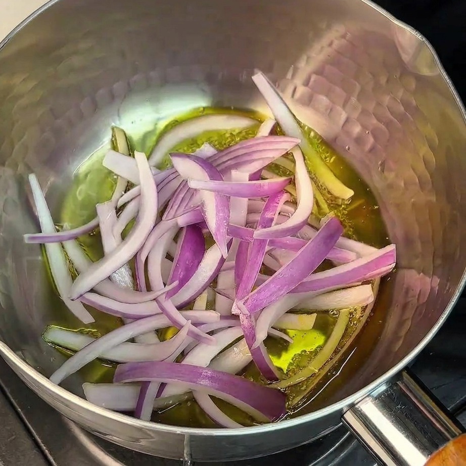 Cipolle rosse affettate sottilmente soffritte in olio sul fondo di una pentola in acciaio inox.