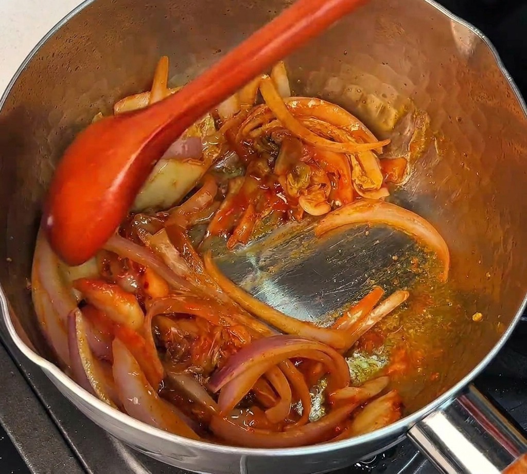 Un cucchiaio di legno mescola kimchi tritato e cipolle rosse in una pentola calda.