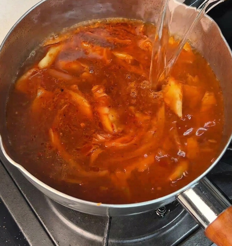 Un getto di acqua bollente versato in una pentola con una base rossa piccante che bolle.