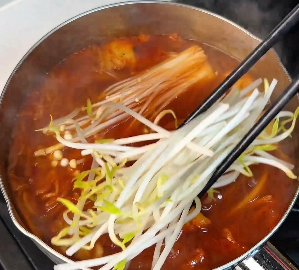 Germogli di soia freschi aggiunti con le bacchette nella zuppa rossa bollente insieme ai funghi enoki.