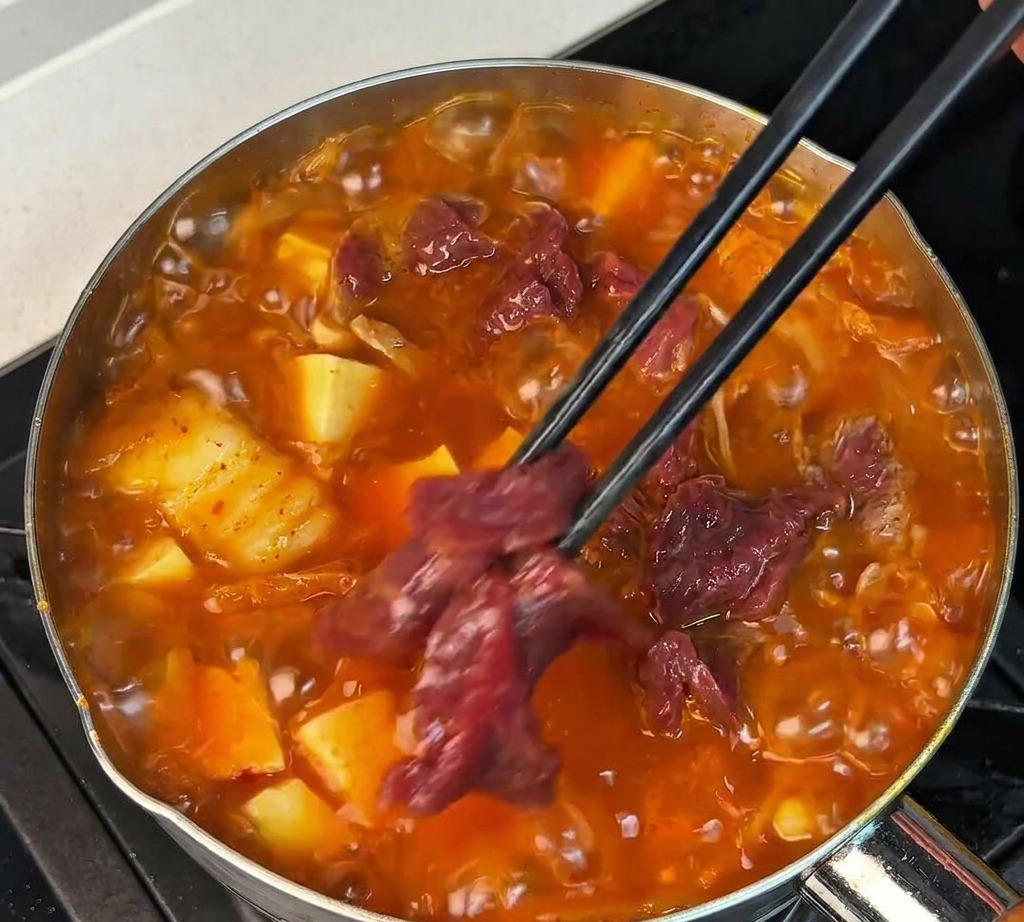 Fette di manzo crudo marinato immerse in una zuppa rossa bollente con bacchette nere.