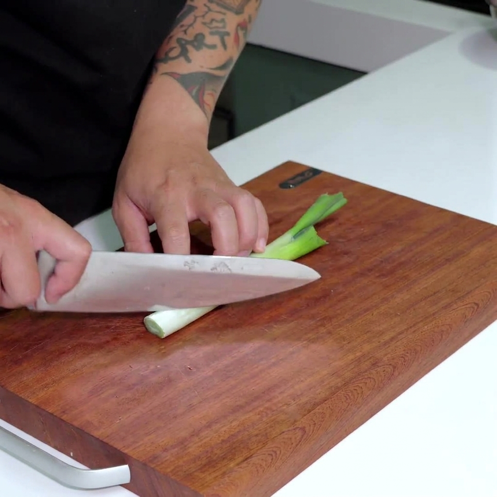Un coltello che affetta la parte bianca di un porro fresco a rondelle sottili su una superficie di legno.