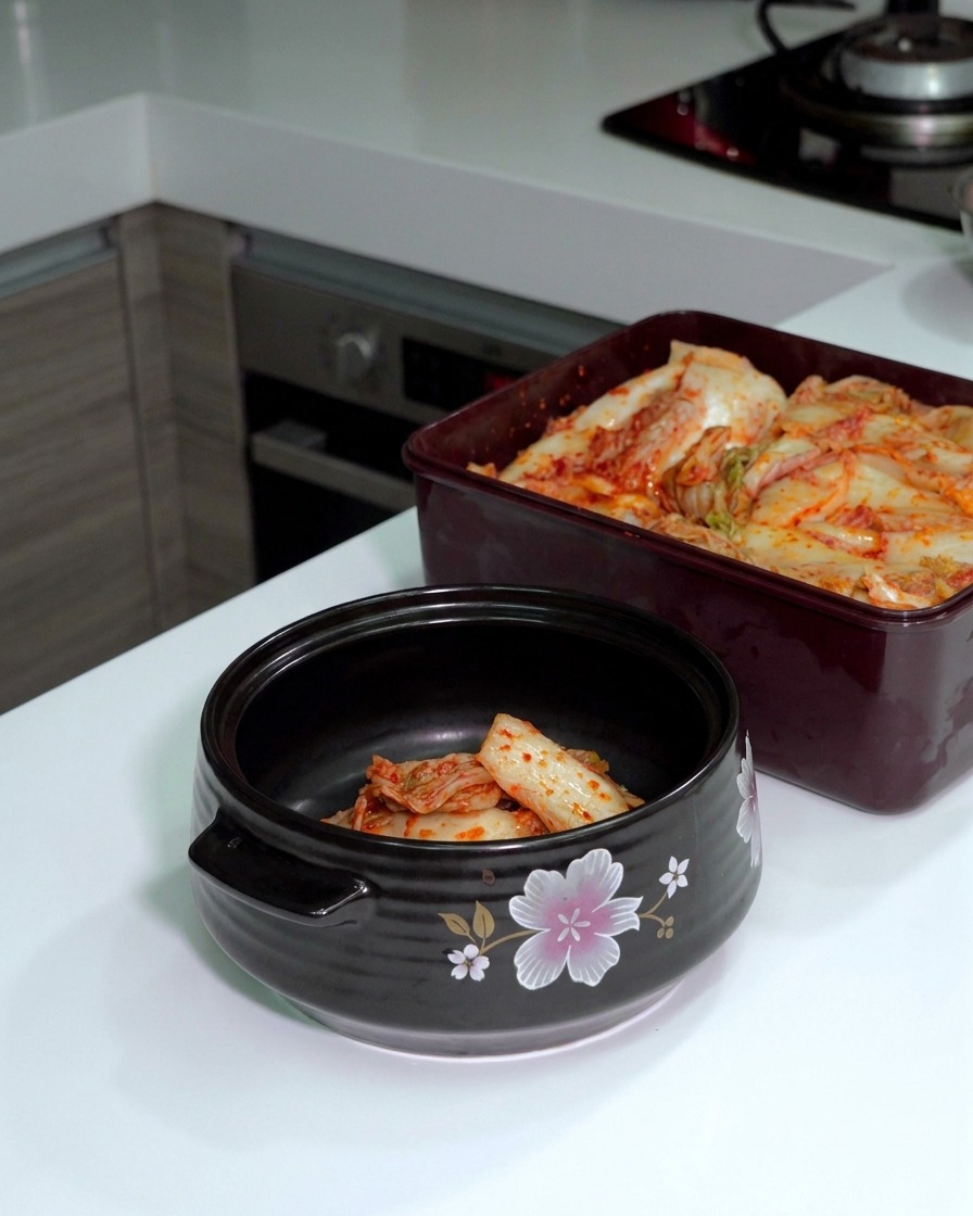 Kimchi di cavolo fermentato tagliato con forbici dargento allinterno di una pentola di ceramica scura.
