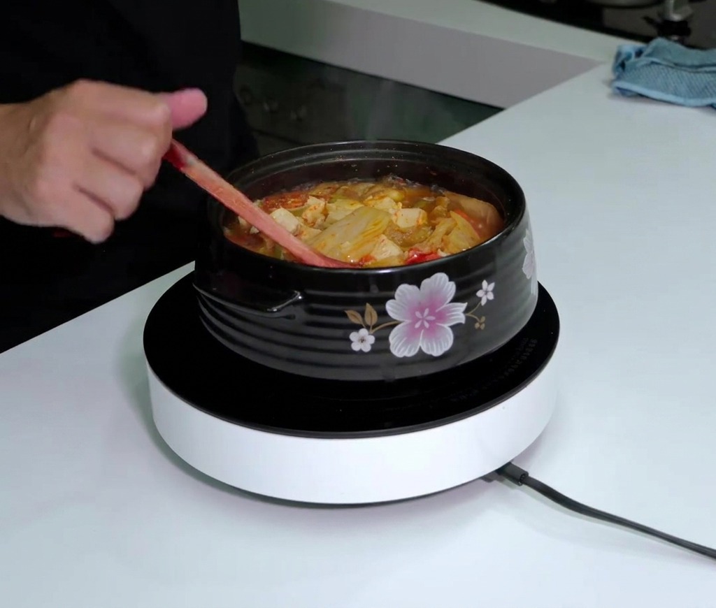 Una bottiglia di Tabasco sopra una pentola di zuppa di kimchi fumante e bollente mentre viene mescolata.