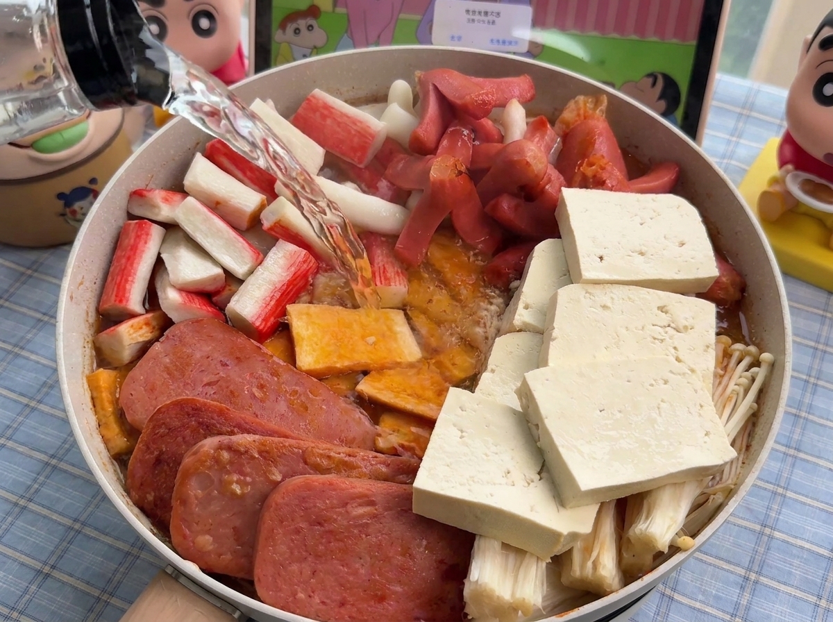 Acqua calda versata da una bottiglia in una padella piena di ingredienti per la zuppa ben disposti.