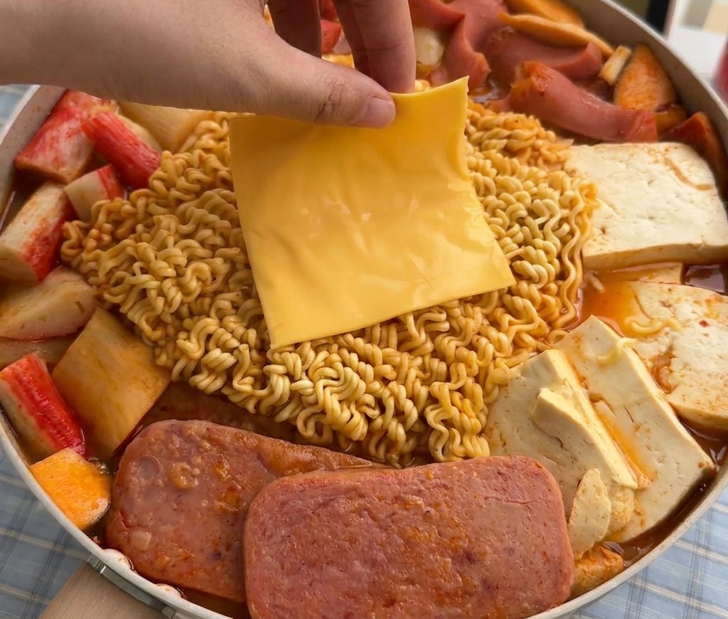 Una mano che mette una fetta di formaggio giallo sopra i noodles che si ammorbidiscono nella zuppa fumante.