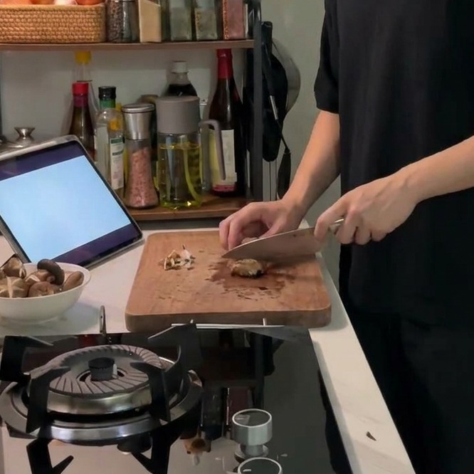 Un coltello affilato che incide un motivo a croce decorativo sulla cappella di un fungo shiitake fresco su un tagliere di legno.