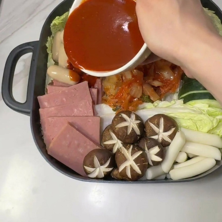 Salsa gochujang rossa piccante versata da una ciotola bianca al centro degli ingredienti crudi dello stufato.