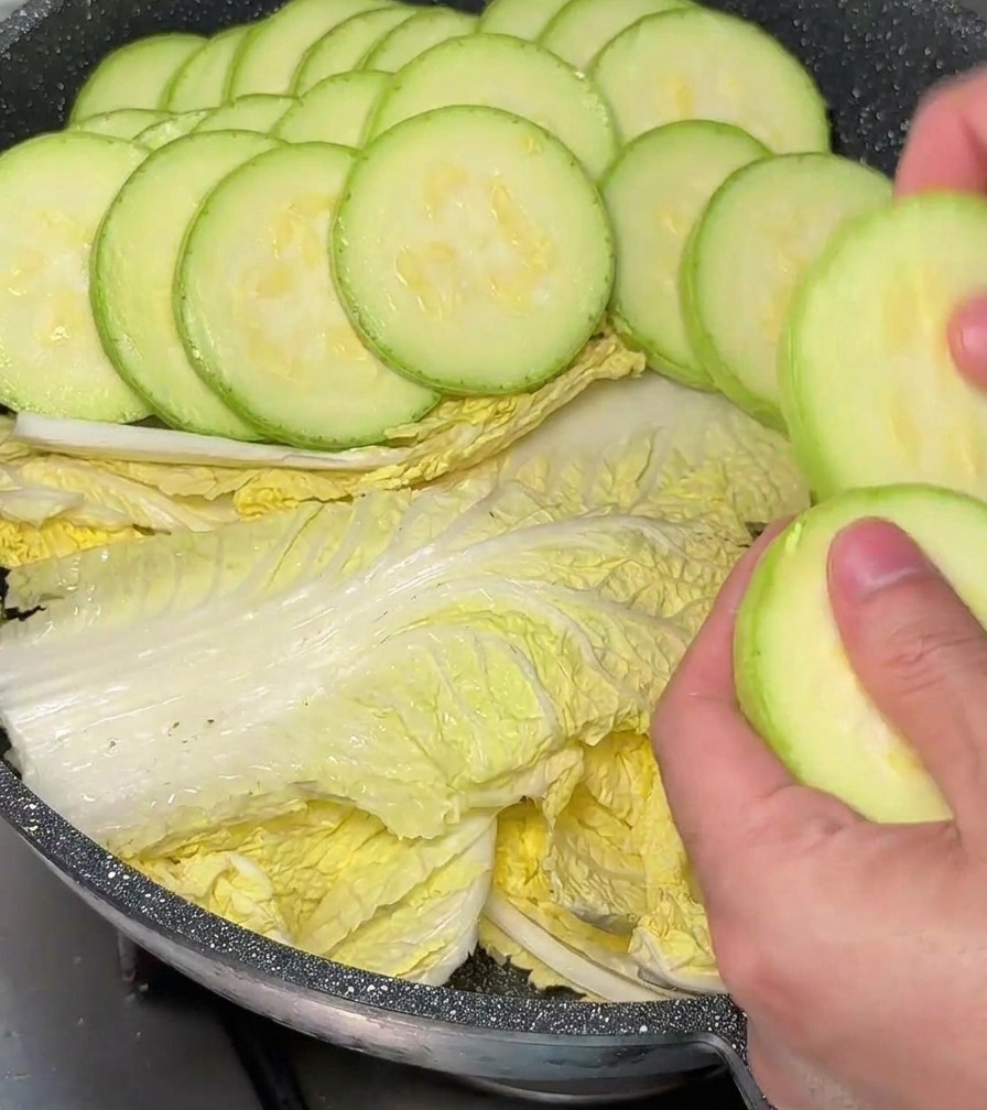 Mani che posizionano con cura rondelle di zucchina in modo circolare sopra il cavolo in pentola.
