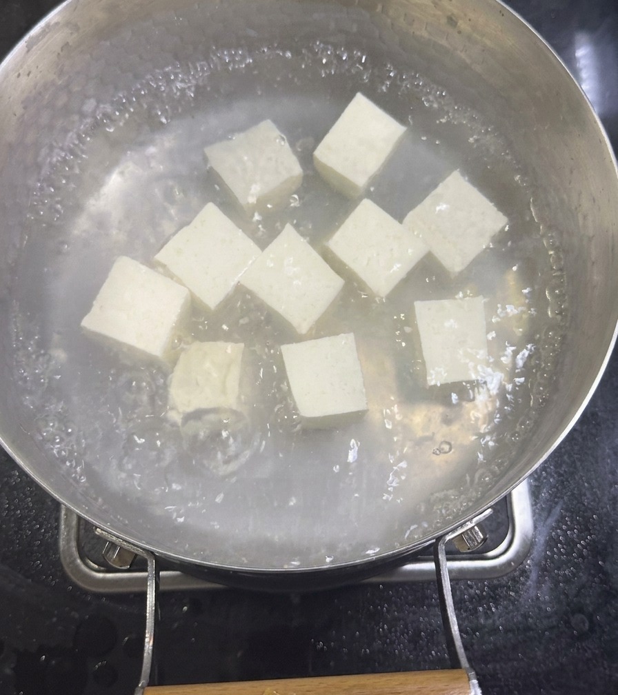 Cubetti di tofu vellutato bianco che sobbollono in una pentola di brodo di vongole diluito sul fornello.