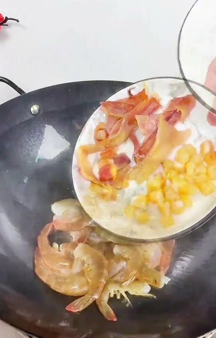 Una persona che versa un piatto di calamari affettati e capesante essiccate in un wok scuro contenente gamberi freschi e listarelle di zenzero.