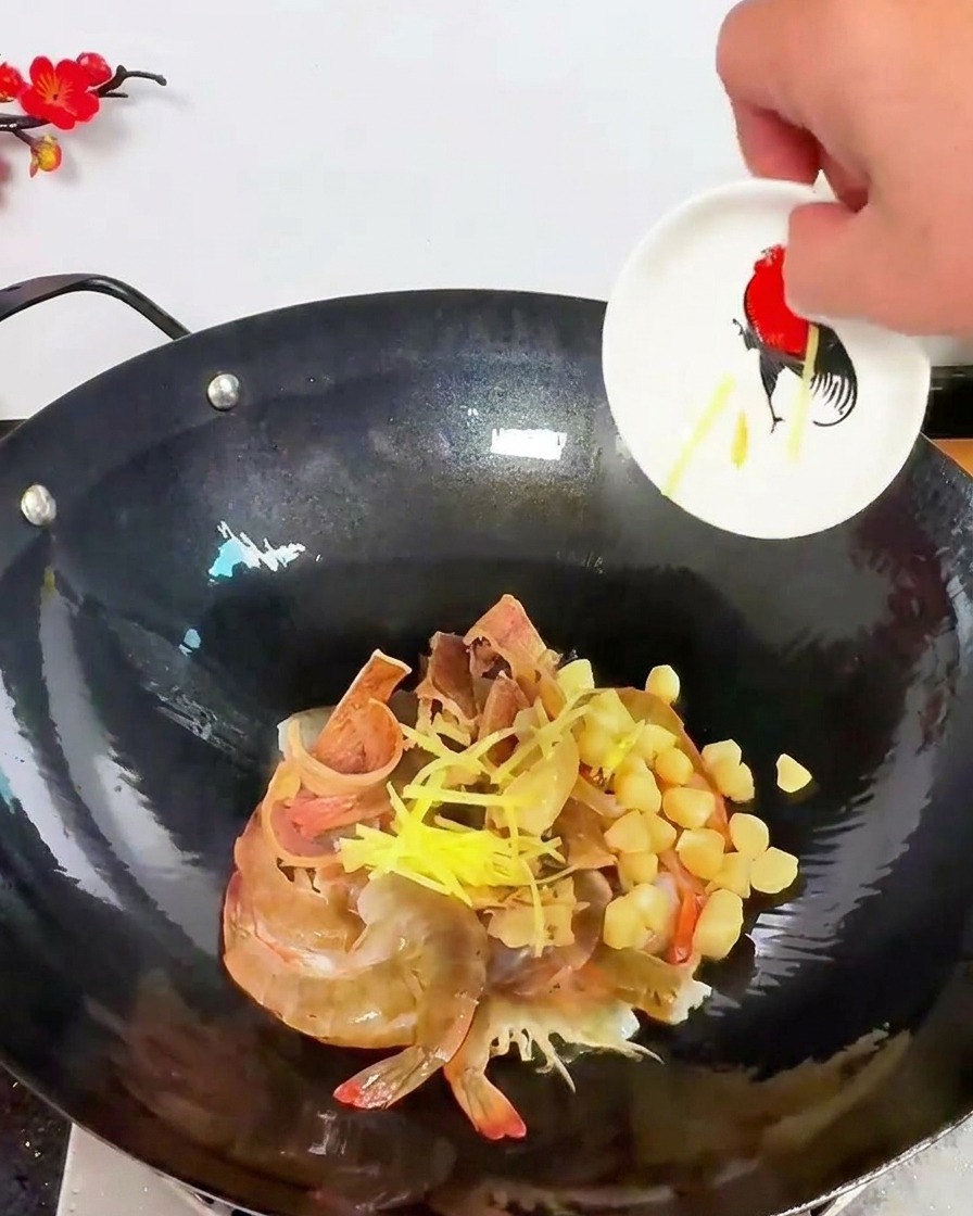 Listarelle di zenzero giallo brillante sparse su un mix di gamberi crudi e capesante essiccate in un wok scuro.