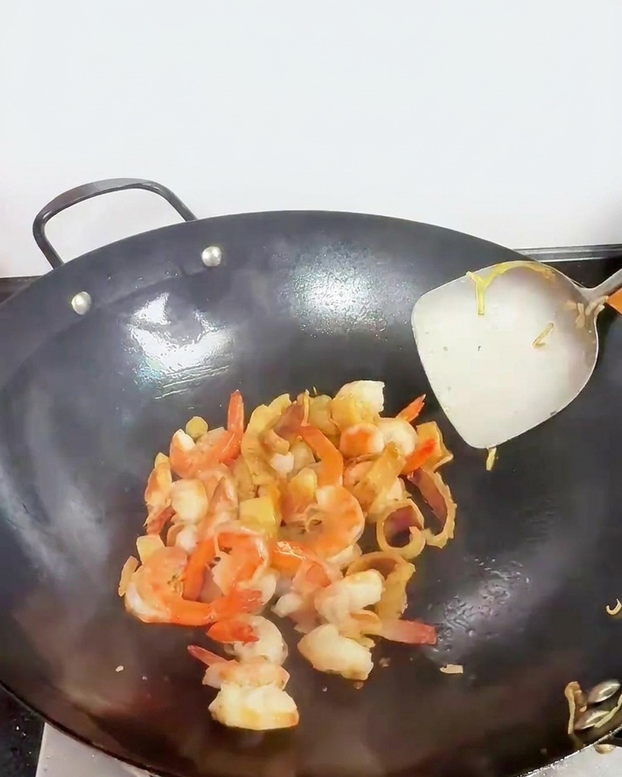 Pezzi di frutti di mare, inclusi gamberi di colore rosa, saltati in un wok con una spatola di metallo.