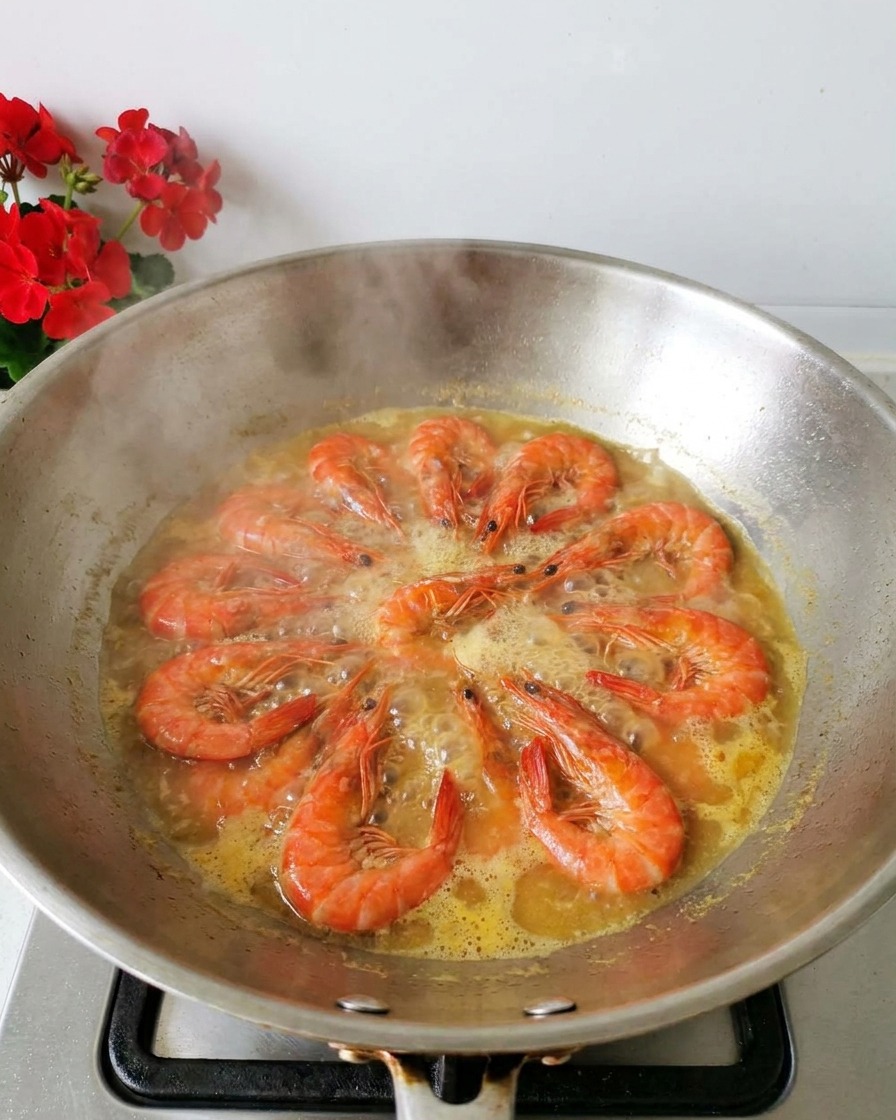 Gamberi arancioni freschi che bollono in un brodo giallo chiaro allinterno di un wok in acciaio inossidabile con vapore che sale.