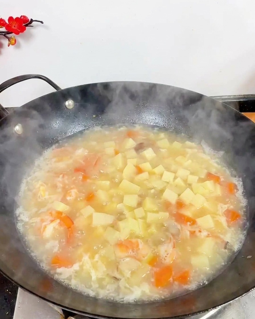 Vista dallalto di un wok pieno di zuppa bianca bollente, con molti cubetti di tofu bianco, gamberi e piccoli funghi marroni.