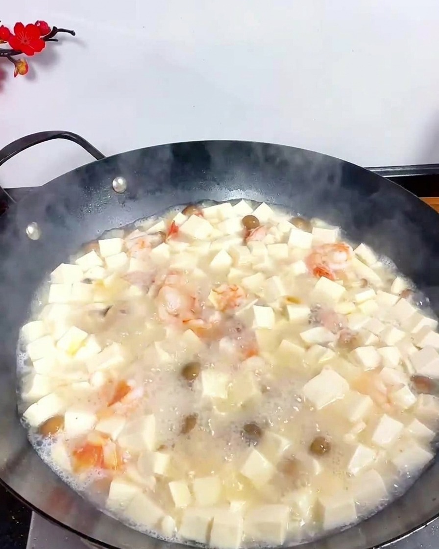 Un cucchiaio di metallo che spolvera pepe bianco in polvere in una zuppa di tofu e frutti di mare bollente in un wok nero.