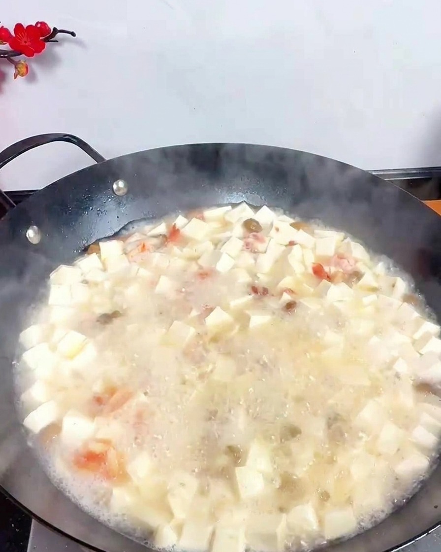 Un mestolo in acciaio inossidabile che versa aceto scuro in una zuppa bianca bollente piena di tofu e frutti di mare.