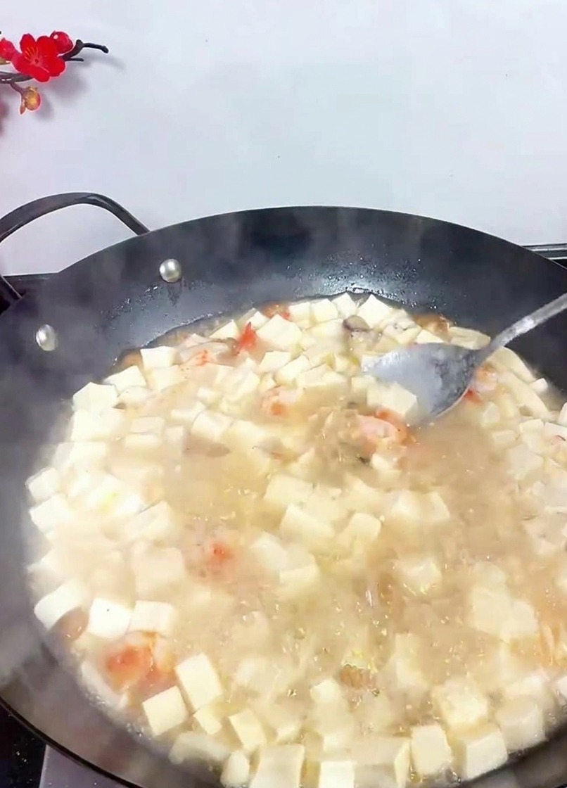 Un cucchiaio che mescola un wok di zuppa di tofu bianco bollente per incorporare i condimenti aggiunti.