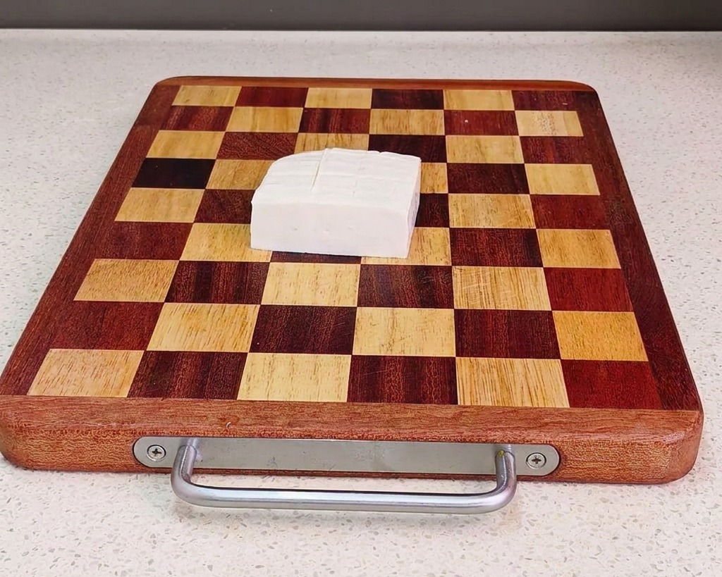 Un panetto di tofu bianco tagliato a cubetti uniformi su un tagliere di legno a scacchi.