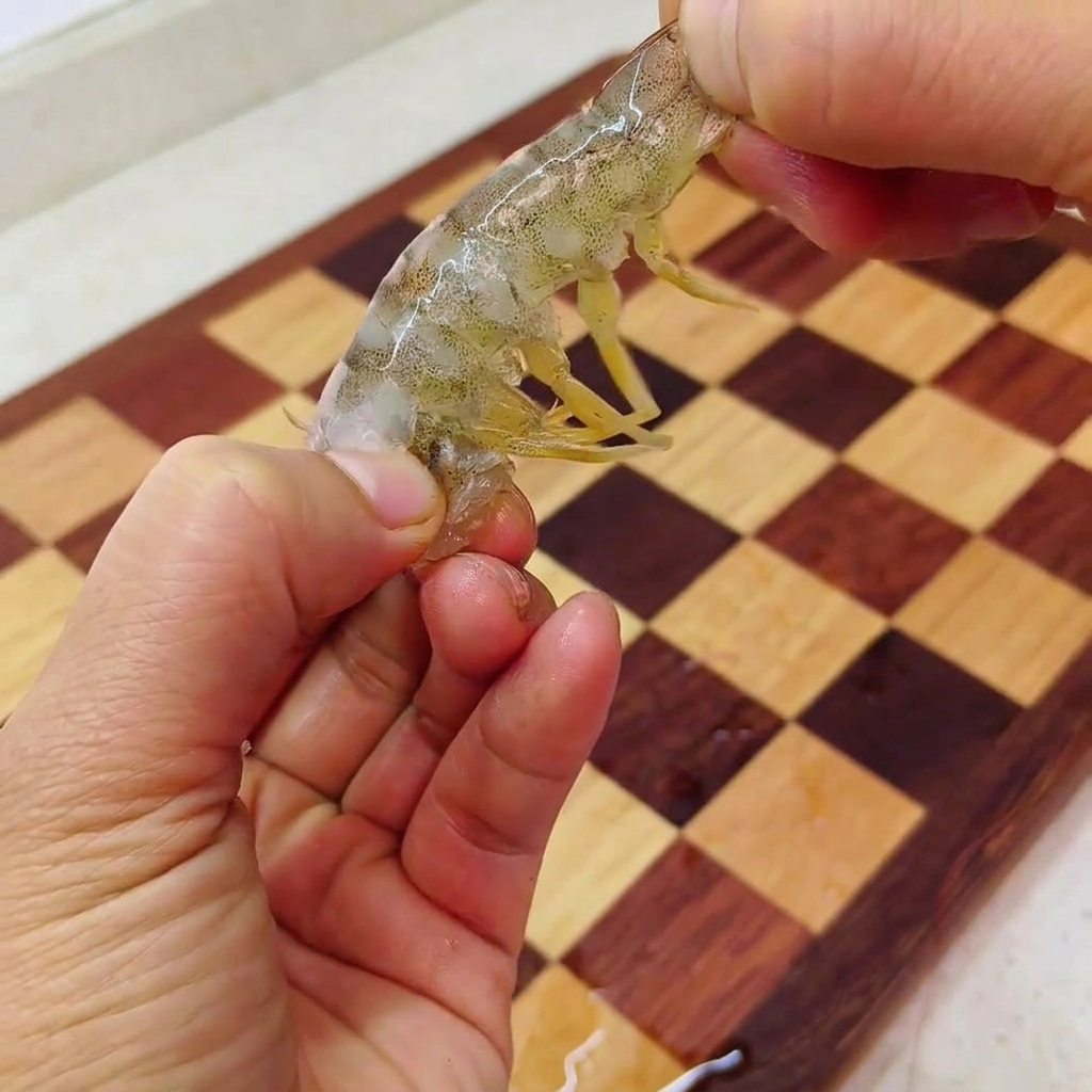 Mani che tengono un gambero parzialmente sbucciato estraendo la polpa dal guscio della coda.