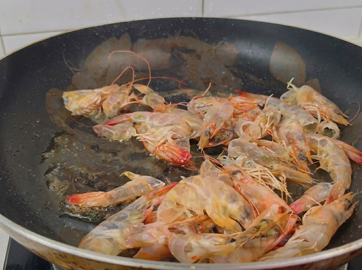 Una padella con gusci di gambero che vengono soffritti in olio fino a diventare di un arancione vivace.