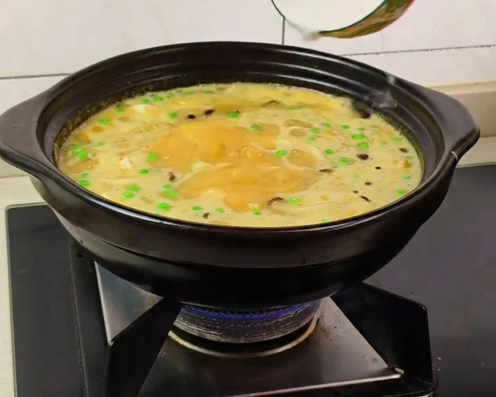 Una mano che versa lamido sciolto in acqua in una zuppa gialla bollente con piselli e funghi.