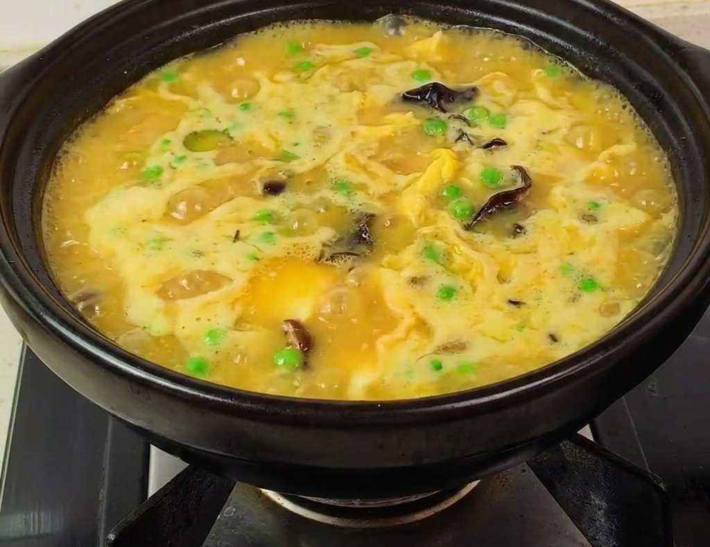 Pentola di terracotta con zuppa gialla densa, gamberi, piselli e funghi pronta sul fornello.
