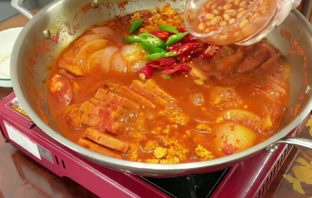 Una mano versa fagioli stufati in una pentola bollente che contiene già peperoncini rossi e verdi a fette.