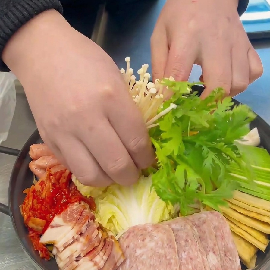 Mani che posizionano con cura un mazzetto di funghi enoki bianchi e foglie verdi di ghirlanda di margherite al centro della pentola.