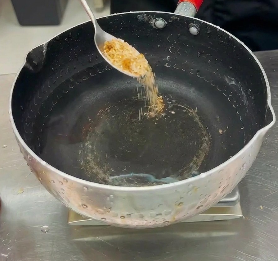 Polvere di condimento versata da un cucchiaio in una pentola dacqua per preparare il brodo dello stufato.