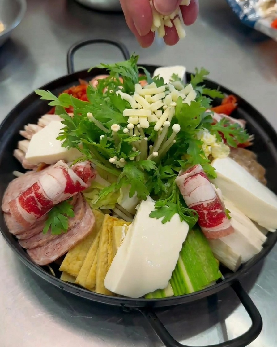Primo piano di formaggio bianco grattugiato spolverato a mano sopra una pentola colorata di Budae-jjigae.