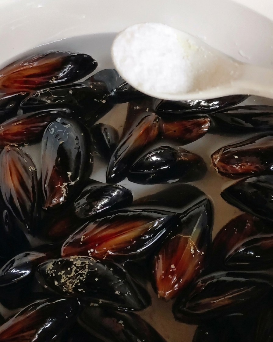 Un cucchiaio di sale aggiunto a una pentola di cozze nere immerse in acqua.