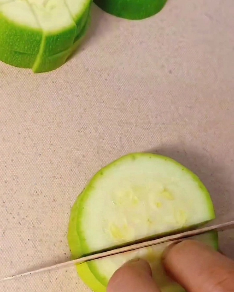 Primo piano di una mano che taglia una zucchina verde a cubetti regolari su un tagliere.