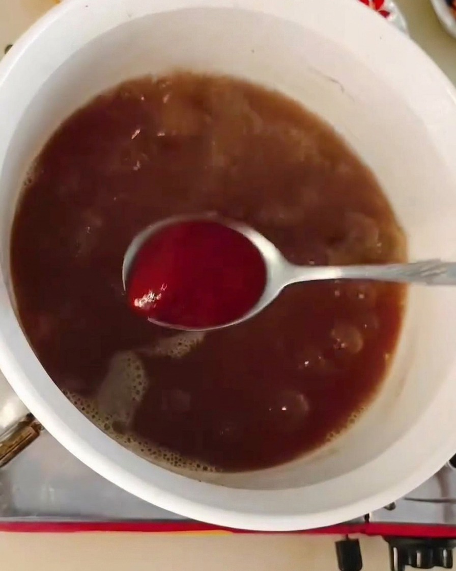 Un cucchiaio di pasta di peperoncino rossa mescolato in una pentola di brodo marrone scuro.