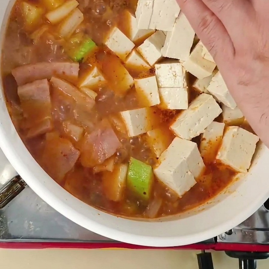 Una mano che adagia cubetti di tofu bianco fresco in uno stufato bollente con zucchine.