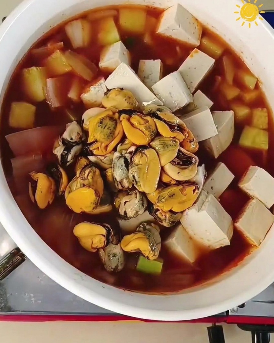 Polpa di cozze e gamberoni crudi aggiunti al centro di una pentola bollente con tofu e verdure.