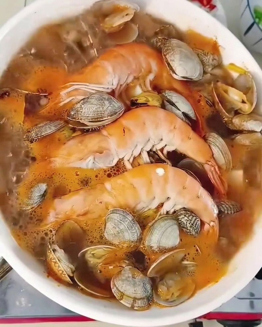 Primo piano di uno stufato di pesce bollente con gamberi, vongole e tofu, guarnito con peperoncini e cipollotti.