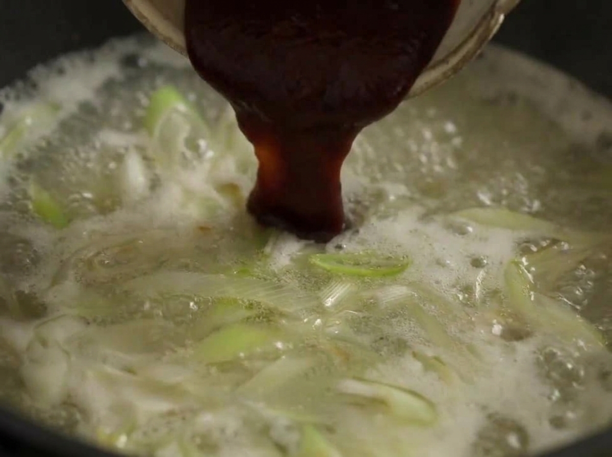 Un grande cucchiaio di pasta di peperoncino rosso mescolato in una pentola di brodo bollente con porri.