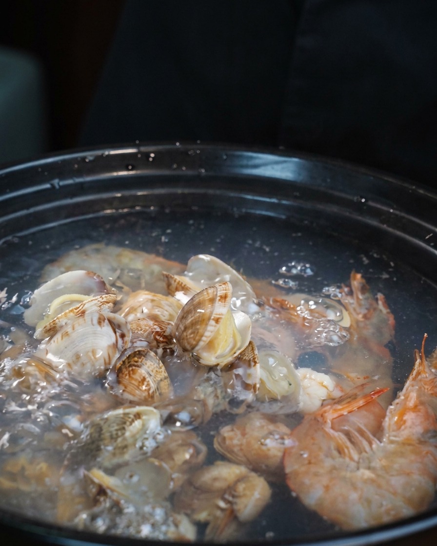 Pezzi chiari di tentacoli di polpo crudi aggiunti alla pentola di zuppa di pesce bollente.