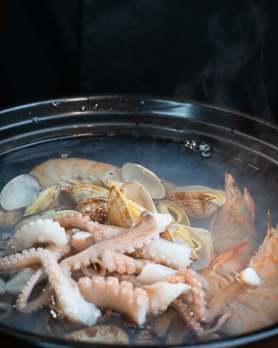 Fette di tofu bianco adagiate sopra il polpo e le vongole nella pentola che sobbolle.