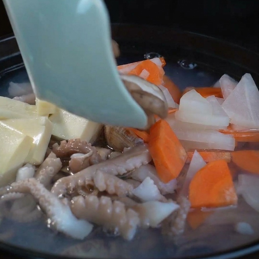 Fette di funghi shiitake freschi aggiunti a una zuppa di pesce gorgogliante insieme a tofu e verdure.